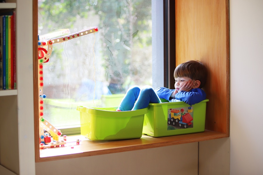 Kind sitzt gelangweilt am Fenster