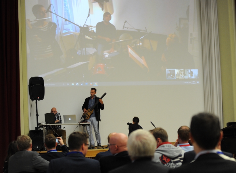 Musiker auf der Bühne und Musiker im Hintergrund auf einem Flatscreen musizieren gemeinsam.